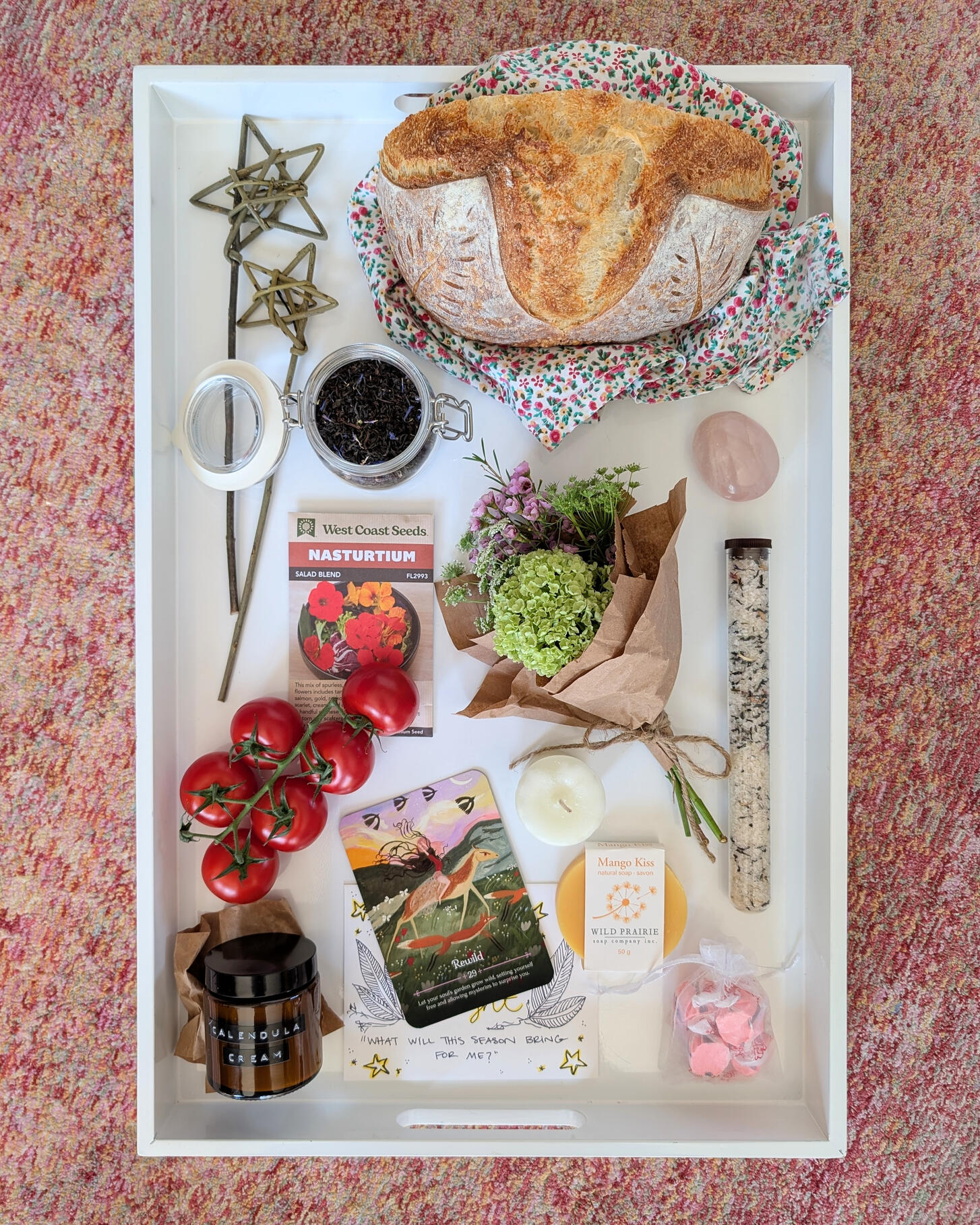 Gathering Table Examples Display of items, fresh bread, tomatoes, flowers, candles, tea, seed packet, soap.