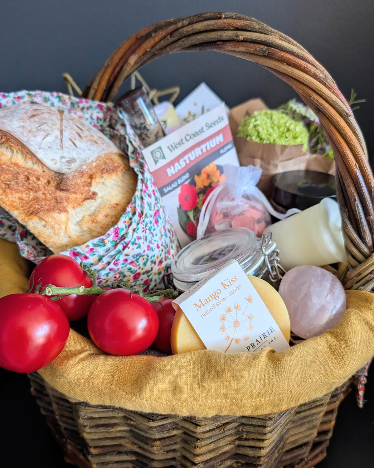 WIllow basket full of the collected items, tomatoes, bread, soap, candles, flowers.