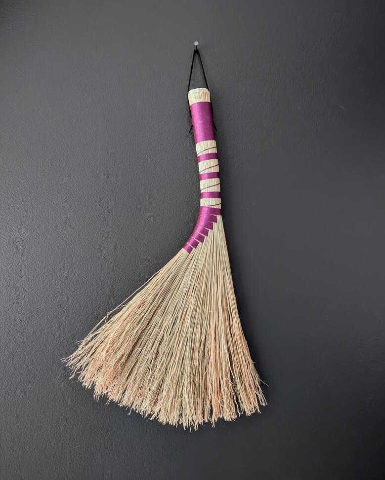 Turkey Wing Handbroom A handbroom bound in purple twine, hanging on the wall.