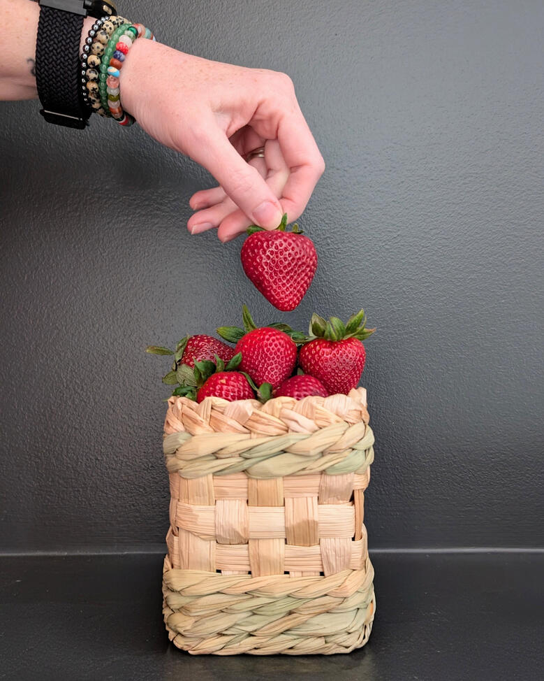 Cattail Berry Basket Woven cattail berry basket, full of strawberries with a hand picking one up.