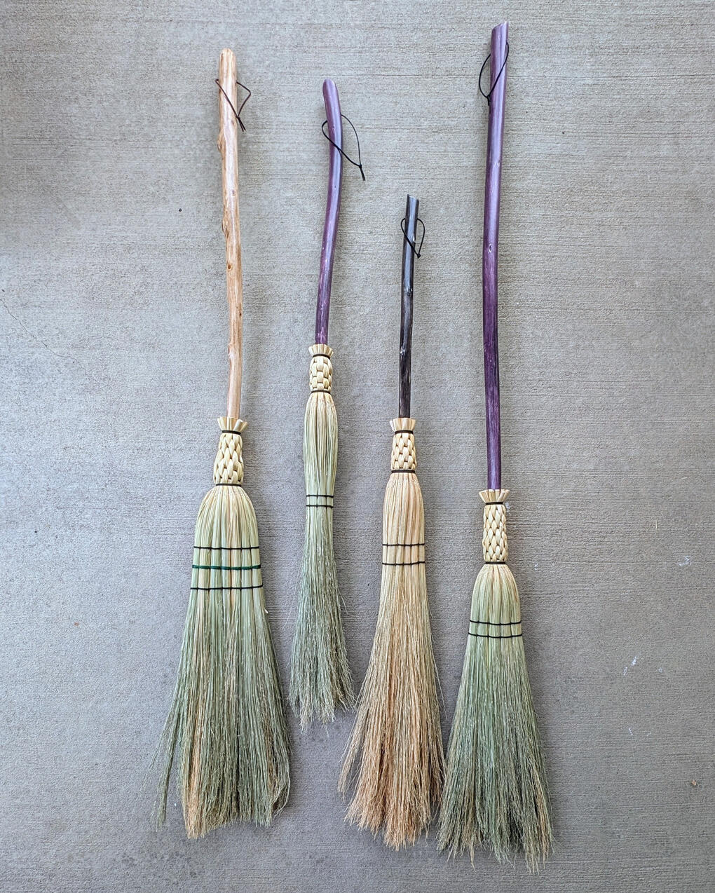 Four brooms lined up on a concrete background.