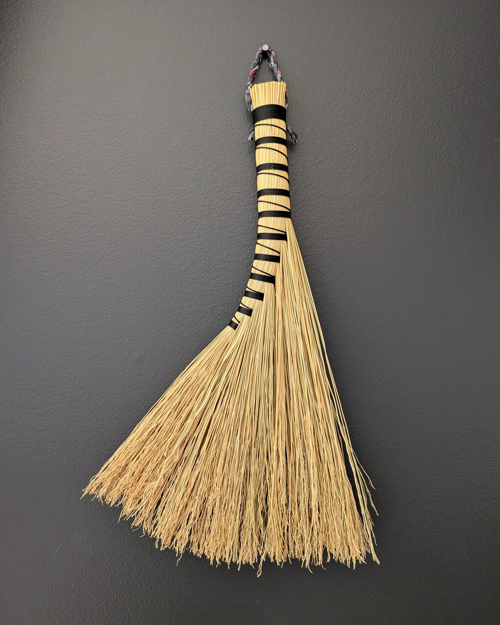 A handbroom bound in black twine, hanging on the wall.