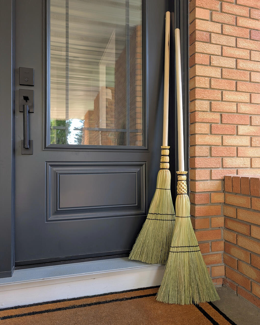 Two sweeper brooms leaning against a black door and orange brick.
