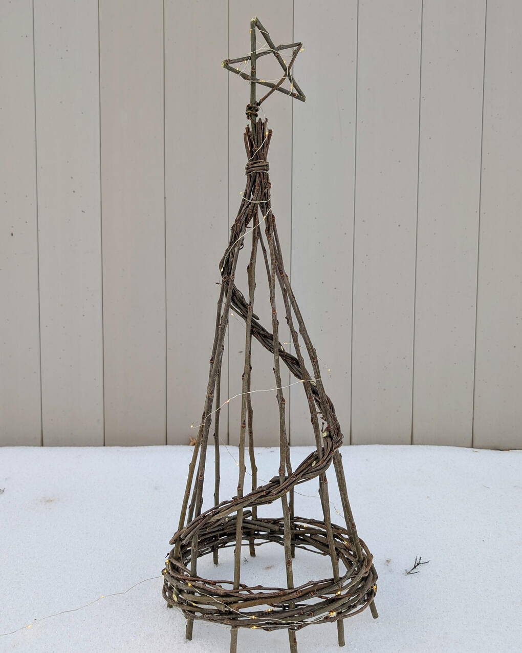 Willow spiral tree with lights and star on top, in the snow.